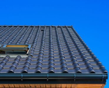 A vertical low angle closeup shot of the black roof of a building with a blue background